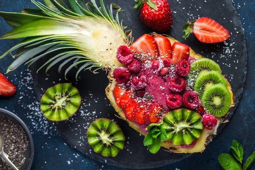 Ananashälfte gefüllt mit Smoothie und Obst, Kiwi, Erdbeere, Himbeere und Granatapfel.