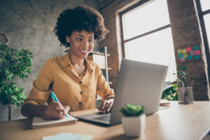 Frau, die am Laptop eine Coaching Website besucht und sich auf einem Notizblock Notizen macht
