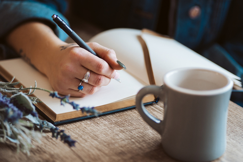 Frau, die mit einem Stift in der Hand in einem Buch etwas aufschreibt.