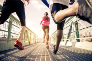 Personen joggen auf einer Brücke, ganz vorne läuft eine Frau. Ausdauertraining