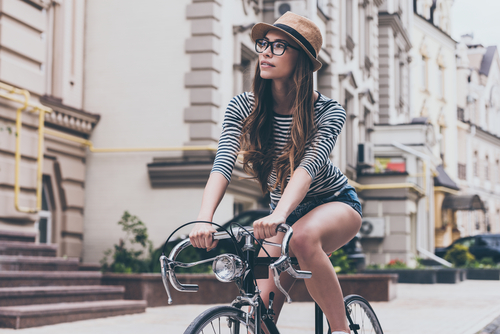 Frau mit Hut und Brille fährt in der Stadt Fahrrad.