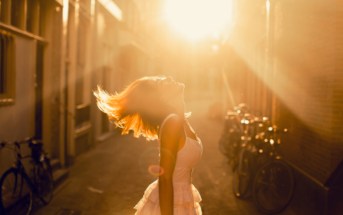 Frau, die mitten in einer Gasse glücklich nach oben zur Sonne blickt.