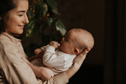 Frau hält Baby im Arm, schaut es an und lächelt.