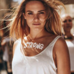Blonde Frau ist bei Demo, auf ihrer Brust steht das Wort Strong in weißen Buchstaben.