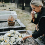 Frau steht weinend an Grab. Abschied nehmen bei Beerdigung