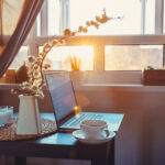 Stillleben, auf einem kleinen Tisch steht ein Laptop, eine Tasse und Vase mit Blumen