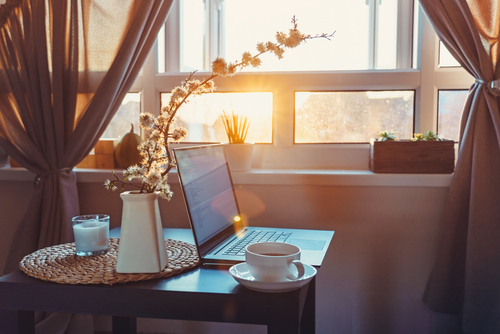 Stillleben, auf einem kleinen Tisch steht ein Laptop, eine Tasse und Vase mit Blumen