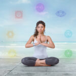 Frau sitzt in Meditationhaltung, um sie herum sind 7 Chakren. Frau macht Chakra Arbeit.