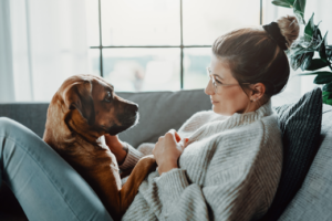 Frau sitzt mit braunem Hund auf Sofa. Tierkommunikation