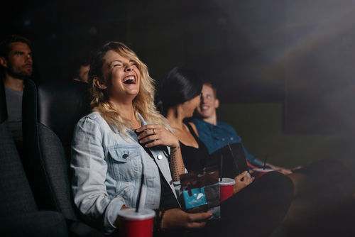 Frau sitzt mit Freunden im Kino, schaut einen Film und lacht