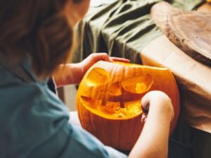 Frau schnitzt ein Halloween Gesicht in den orangen Kürbis