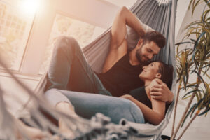 Liebespaar in der Hängematte im Zimmer, Mann hält Frau im Arm.