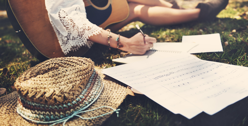 Frau sitzt mit Gitarre im Gras und schreibt Noten und Texte - Songwriter