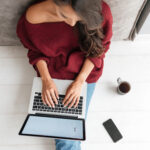 Frau sitzt am Laptop vor Website und tippt auf der Tastatur