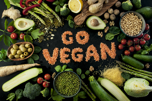 Mit roten Linsen auf schwarzem Hintergrund steht der Satz Go Vegan, drumherum liegen Gemüse, Obst, Kerne, Samen und Hülsenfrüchte
