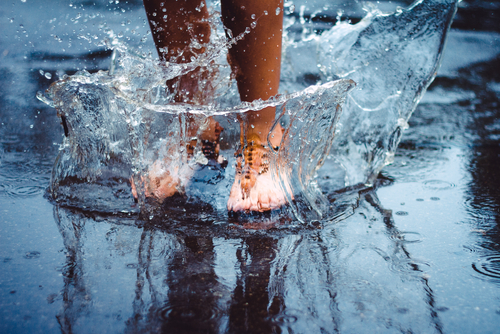 Barfuß in eine Pfütze springen, das Wasser spritz zu allen Seiten hoch.