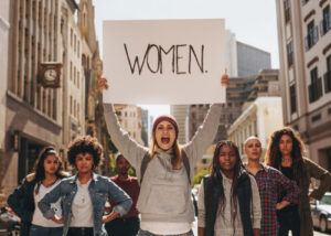 Frau hält bei einer Demonstration für Frauenrechte ein Plakat mit der Aufschrift ‚Women‘ hoch - Solidarität unter Frauen